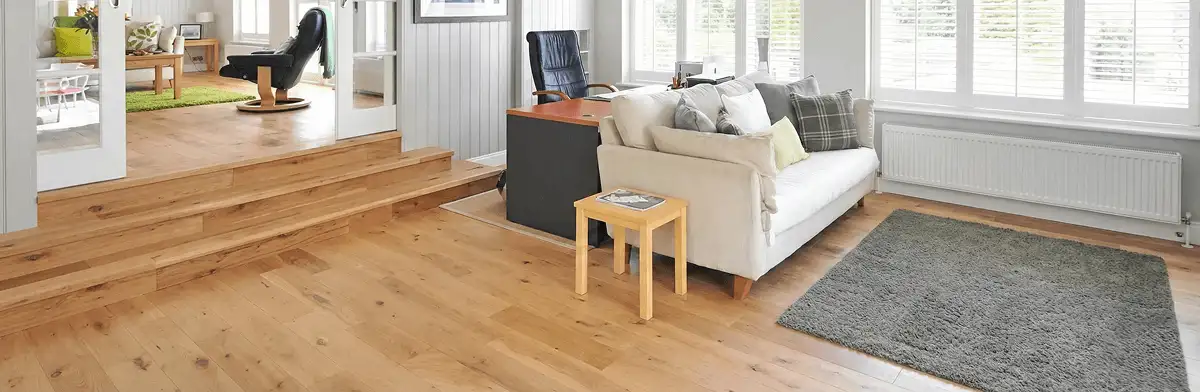 A modern living room with professionally installed laminate flooring, a beige sofa, a small side table, a gray rug, and large windows with white shutters in Newark, NJ